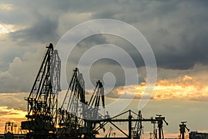 Silhouette of port cranes against a dramatic sky at sunset.