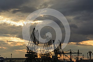 Silhouette of port cranes against a dramatic sky at sunset.