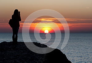 Silhouette portrait of female watching and take a photo with beautiful sunset at the sea background, Sea & sunset over sea horizon