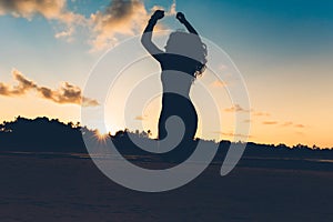 silhouette portrait of summer girl jumping with hands in air on white sand in exotic island at sunset.