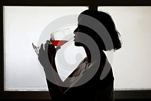 Silhouette portrait of woman with the red wine in the glass near the window with natural lighting. Dark tone
