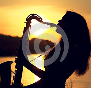 The silhouette portrait of a young woman who skillfully playing the saxophone in the nature that gives her peace of tranquility