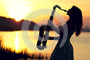 The silhouette portrait of a young woman who skillfully playing the saxophone in the nature that gives her peace of tranquility