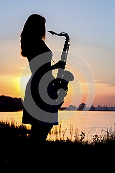 The silhouette portrait of a young woman who skillfully playing the saxophone in the nature that gives her peace of tranquility