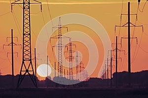 Silhouette of a power line during sunset, the sun and electric metal supports extending into the distance beyond the horizon