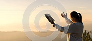 Silhouette of prayer woman worship to God with bible in morning on sunrise sky background. Person hands open palm up worship. God