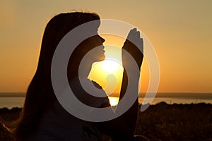 Silhouette of a praying girl at sunset