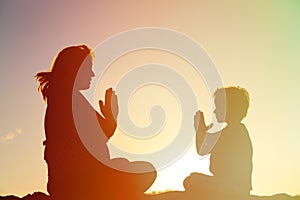 Silhouette of pregnant mother and son doing yoga on beach