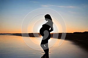 Silhouette of a pregnant woman on beach at sunset.