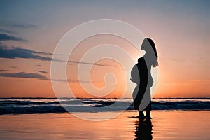Silhouette of a pregnant woman on beach at sunset.