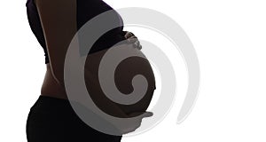 Silhouette of pregnant woman`s belly with hands touching it on white isolated background, new life concept