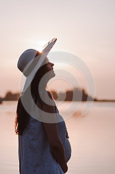 The silhouette of a pregnant woman at sunset.The silhouette of a peaceful, happy woman in a straw hat holding her