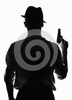 Silhouette of private detective with a gun in right hand. Agent stay back to camera. Criminal scene in black and white