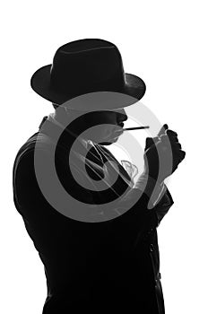 Silhouette of private detective lights cigarette. Agent looks like Al Capone stay side to camera. Police criminal scene in black