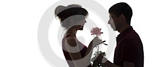 Silhouette profile of a young couple in love on white isolated background, man giving a woman a rose flower, girl is delighted