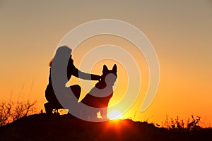 Silhouette profile of young woman embracing German Shepherd dog obediently sitting nearby, girl walking on nature with pet