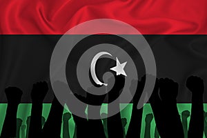 Silhouette of raised arms and clenched fists on the background of the flag of Libya. The concept of power,  conflict. With place