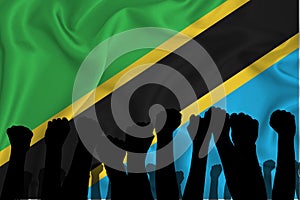 Silhouette of raised arms and clenched fists on the background of the flag of tanzania. The concept of power,  conflict. With
