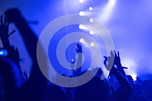 Silhouette of raised arms, crowd of people in the front of bright stage lights at concert