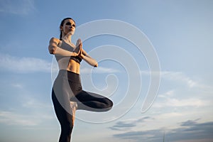 Silhouette rear view of woman doing yoga in tree pose meditating on a rock by the sea with sunset