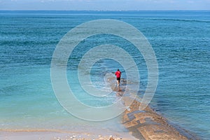 silhouette of a red fisherman at the end of a stone jetty in the middle of the azure blue Atlantic Ocean