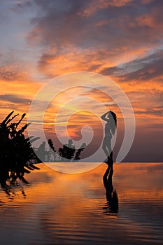 Silhouette and reflection of slim woman on edge infinity luxury pool at sunset