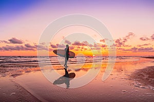 Silhouette and reflection of surfer girl with surfboard on a beach at sunset. Surfer and ocean