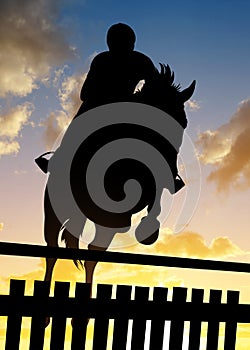 Silhouette of a rider on a horse jumping over obstacle