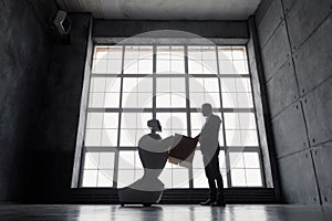 A man communicates with a robot, with cardboard box in hand. delivery concept. silhouette of the robot against the