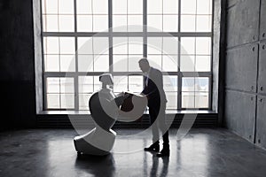 A man communicates with a robot, with cardboard box in hand. delivery concept. silhouette of the robot against the