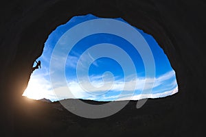 Silhouette of a rock climber climbing an arch shaped rock
