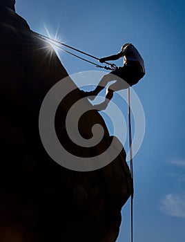 Silhouette of a rock climber repelling on a steep rock boulder against a blue sky