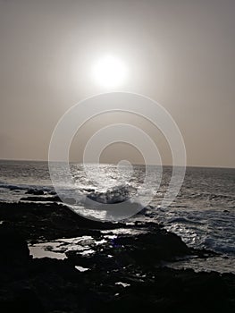 Silhouette of a rocky outcrop with waves splashing and the sun setting in the background