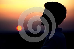 Silhouette of rofile of a young man`s face at sunset in a field