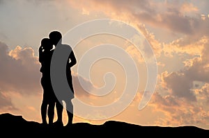 Silhouette of romantic a couple hug kissing against a sunset sky