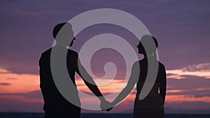 Silhouette romantic couple, a man takes a woman by the hand against the background of a sunset. Romantic couple at