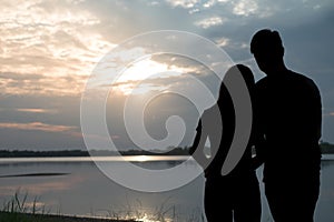 The silhouette of a romantic couple standing, hugging each other and watching the sunset. Romance and love concept