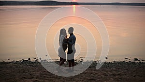 Silhouette of romantic couple walking at lake shore and kissing at sunset.