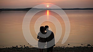 Silhouette of romantic couple walking at lake shore and kissing at sunset.