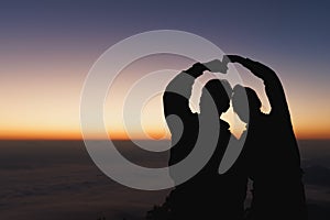 Silhouette  of the romantic scene of the couple sitting on the hill at sunset time. young couple tenderly embracing in the sunset