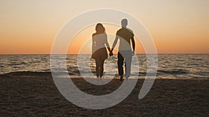 Silhouette of a romantic young couple standing on the seashore, man comes up and takes the girl`s hand and together enjoying sunri