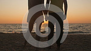 Silhouette of a romantic young couple standing on the seashore, man comes up and takes the girl`s hand and together enjoying sunri