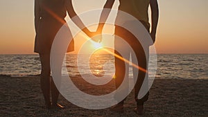 Silhouette of a romantic young couple standing on the seashore, man comes up and takes the girl`s hand and together enjoying sunri