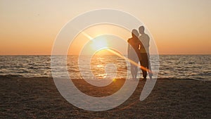 Silhouette of a romantic young couple standing on the seashore, man comes up and takes the girl`s hand and together enjoying sunri