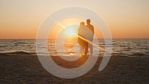 Silhouette of a romantic young couple standing on the seashore, man comes up and takes the girl`s hand and together enjoying sunri