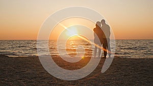 Silhouette of a romantic young couple standing on the seashore, man comes up and takes the girl`s hand and together enjoying sunri