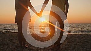 Silhouette of a romantic young couple standing on the seashore, man comes up and takes the girl`s hand and together enjoying sunri