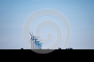 Silhouette of a row of windmills behind each other in the evening