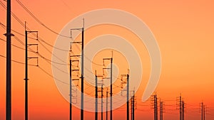 Silhouette rows of electric poles with cable lines against colorful orange sunset sky background, low angle and perspective view