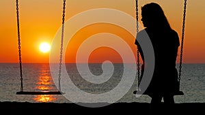 Silhouette of a sad girl swinging looking at side